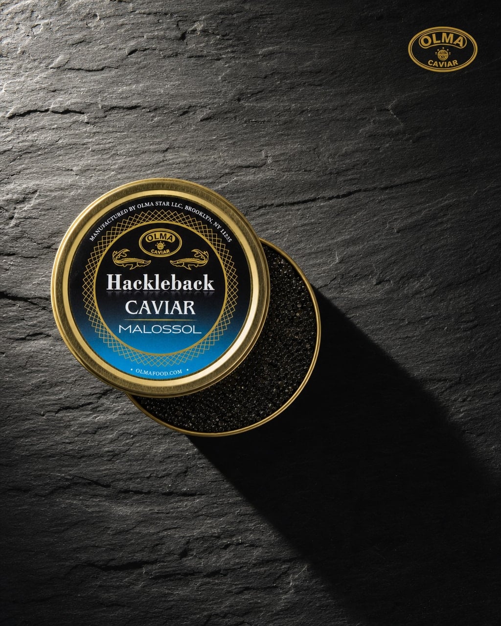 Gold tin of Hackleback Caviar Malossol on a dark slate background with OLMA branding in the corner.