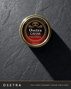 Tin of Osetra caviar on a dark slate surface with a long shadow; label says Osetra Caviar Malossol.