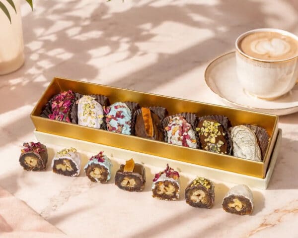 Assorted chocolates in a gold box on a marble surface next to a cup of coffee.